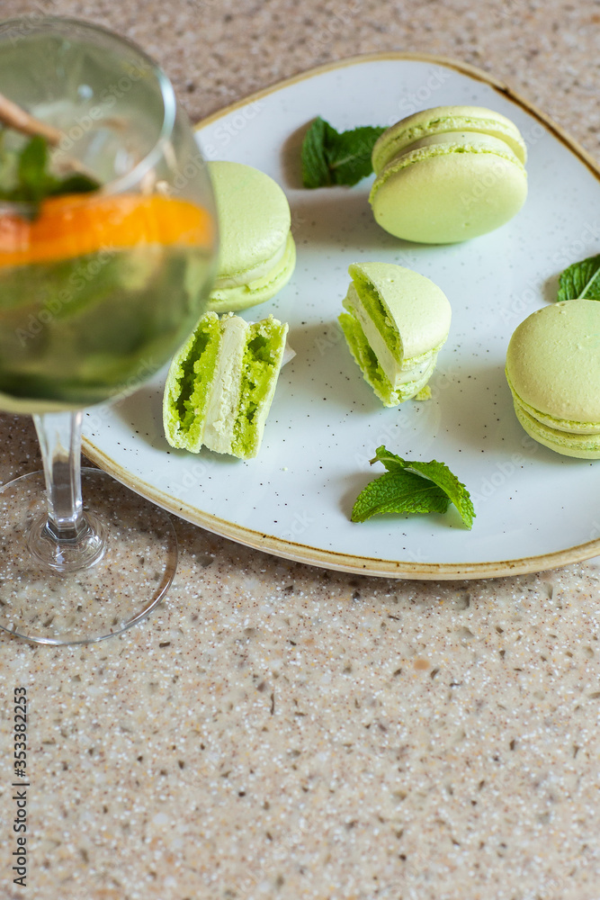 Macaroons on a plate on a gray background. French macarons isolated. Selective focus. Beautiful green macaroons with mint and cocktail. Stylish arrangement sweet. Flat lay, top view. Macro photo. Macaroons on a plate on a gray background. French macarons isolated. Selective focus. Beautiful green macaroons with mint and cocktail. Stylish arrangement sweet. Flat lay, top view. Macro photo.
