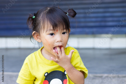 Portrait​ image​ of​ 2-3​ years​ old​ of​ Asian​ baby​ child​ girl​ eating​ and​ sucking, biting​ her​ fingers​ in​ the​ mouth.​ Development​ of​ kid​ concept. photo