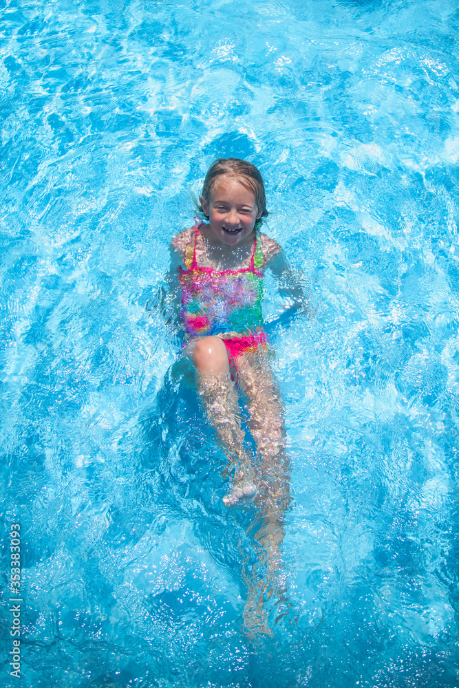 Top view of pretty young girl outdoor in the pool at the resort against blue water. Summer holiday and happy carefree childhood concept.