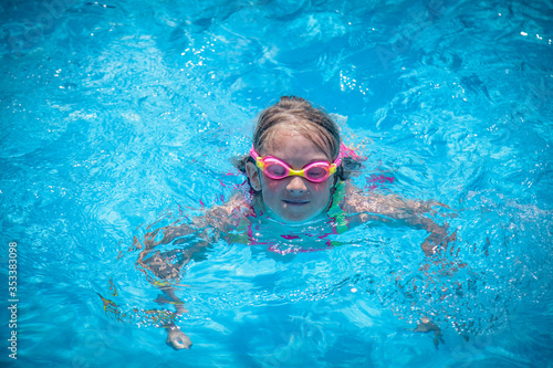 Happy childhood. Young child girl with goggles swimming in pool and having fun leisure activity