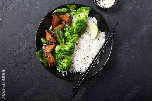 Vegan teryaki  tempeh or tempe buddha bowl  with rice, steamed broccoli, spinach  and lime on black  background. Healthy food