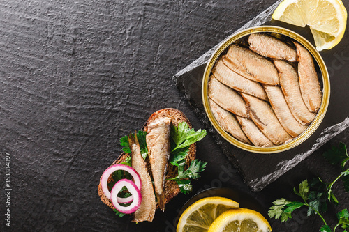 Canvas Print Sprats in tin can and sandwich with sardines, sprats fish with parsley, lemon, spices on rye bread over slate dark background