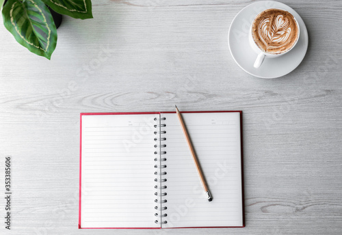 Top view of Notebook with pencil , and cup of coffee on white wooden table.