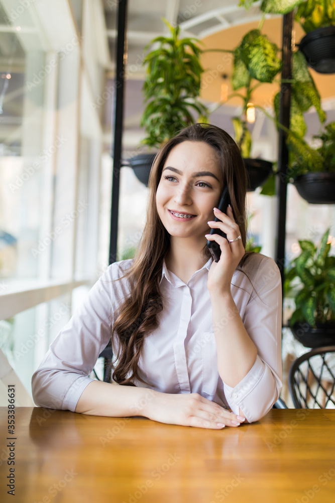 Young happy woman talking on mobile phone with friend while sitting in modern coffee shop Young happy woman talking on mobile phone with friend while sitting in modern coffee shop