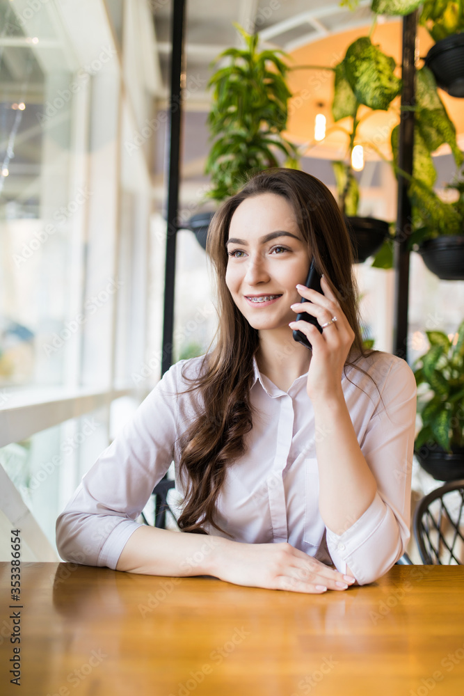 Young charming woman calling with cell telephone while sitting alone in coffee shop during free time Young charming woman calling with cell telephone while sitting alone in coffee shop during free time