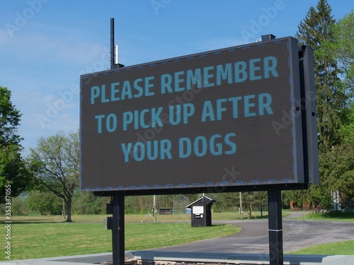 A municipal park sign reminds dog-walkers of the pooper-scooper law requiring them to pick up after their pets