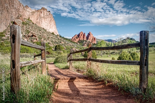 Wood fence frames a hiking trail which leads towards interesting rock formations in Garden of the Gods Park in Colorado Springs.
