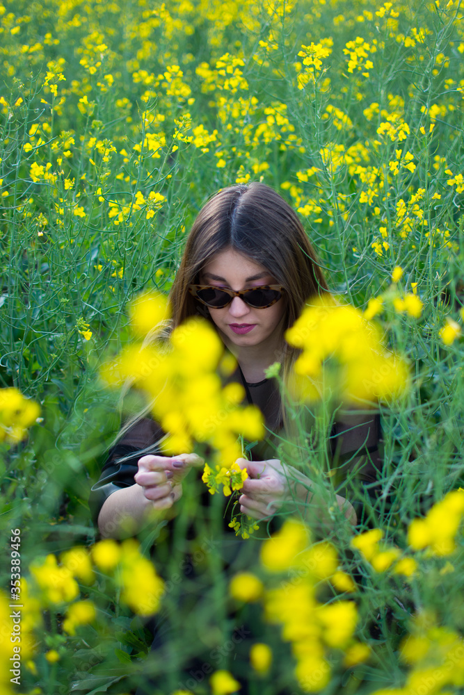 Girl in dark clothes with beautiful hair sitting in a field of yellow rape. Warm spring day Girl in dark clothes with beautiful hair sitting in a field of yellow rape. Warm spring day