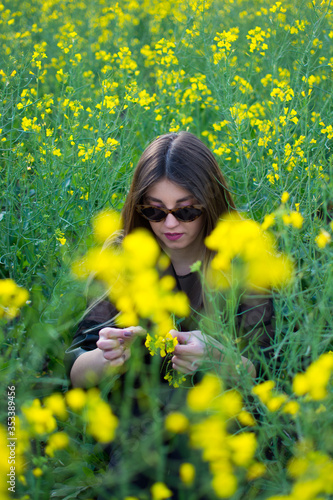 Girl in dark clothes with beautiful hair sitting in a field of yellow rape. Warm spring day