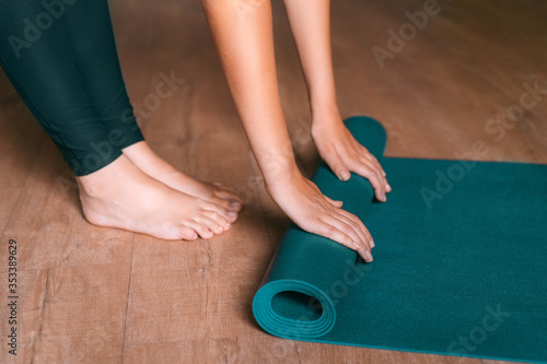 Obraz na plátně Fit woman folding blue exercise mat on wooden floor before or after working out in yoga studio or at home