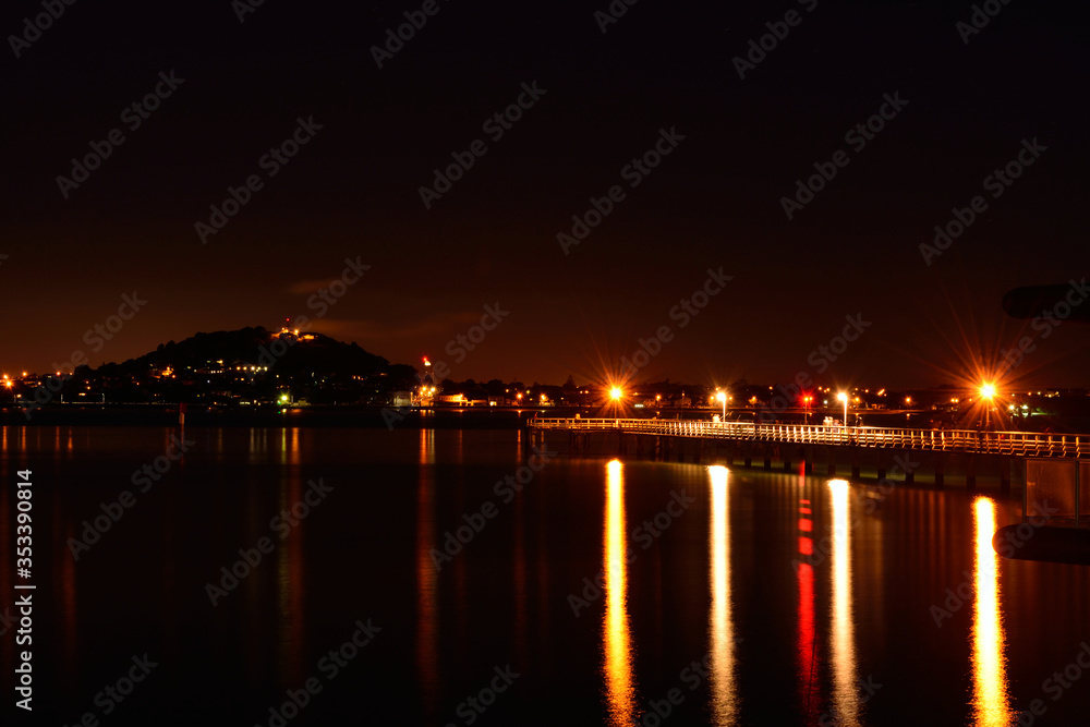 Okahu pier at night: lamp lights, a blurry group of fishermen and a distant silhouette of Mount Victoria
