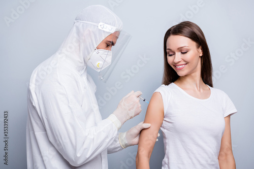 Photo of cheerful patient lady guy expert virology inject shoulder covid antidote experimental vaccine wear mask hood uniform plastic facial protection isolated grey color background