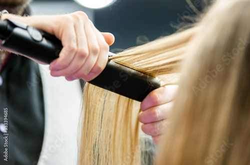 Professional hairdresser straightening long blond hair using straightener