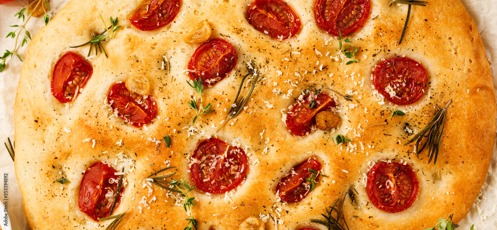 Italian traditional focaccia bread baking with with cherry tomatoes, parmesan and rosemary on light brown background. Top view. Italian traditional focaccia bread baking with with cherry tomatoes, parmesan and rosemary on light brown background. Top view.