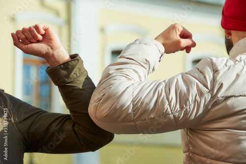 Elbow bumping. Elbow greeting to avoid the spread of coronavirus (COVID-19). A man with a beard and a woman bump elbows instead of greeting with a handshake or hug in the old town.