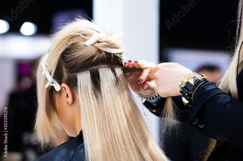 Professional hairdresser making hair extensions for blonde girl in a beauty salon photo