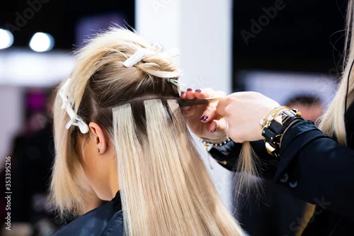 Obraz Professional hairdresser making hair extensions for blonde girl in a beauty salon