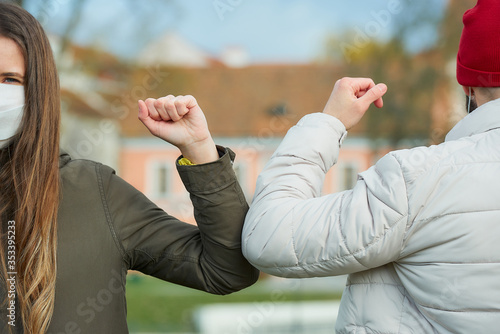 Elbow bumping. Elbow greeting to avoid the spread of coronavirus (COVID-19). A woman and a man in medical masks bump elbows instead of greeting with a hug or handshake in the old town.