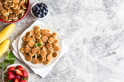 Tiny pancakes for breakfast. Cereal pancakes with blueberries, bananas, strawberries on grey background. Trendy food. Copy space for text or design