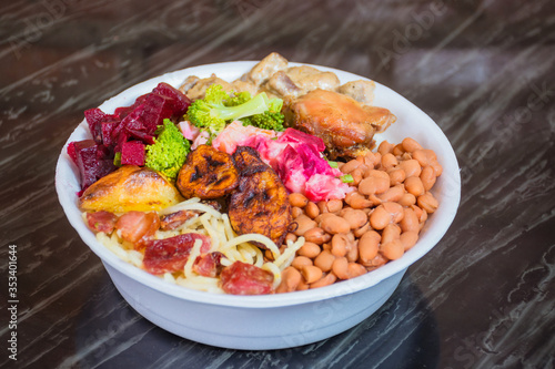 Deliver food, marmita ou marmitex with rice, beans, beets, broccoli, mayonnaise with vegetables, fried chicken, beef stroganoff, pasta and bacon on a dark marble table.