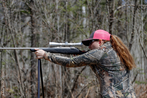 Woman shooting a rifle using shooting sticks.