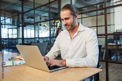 Photo of handsome pleased man working with laptop while sitting