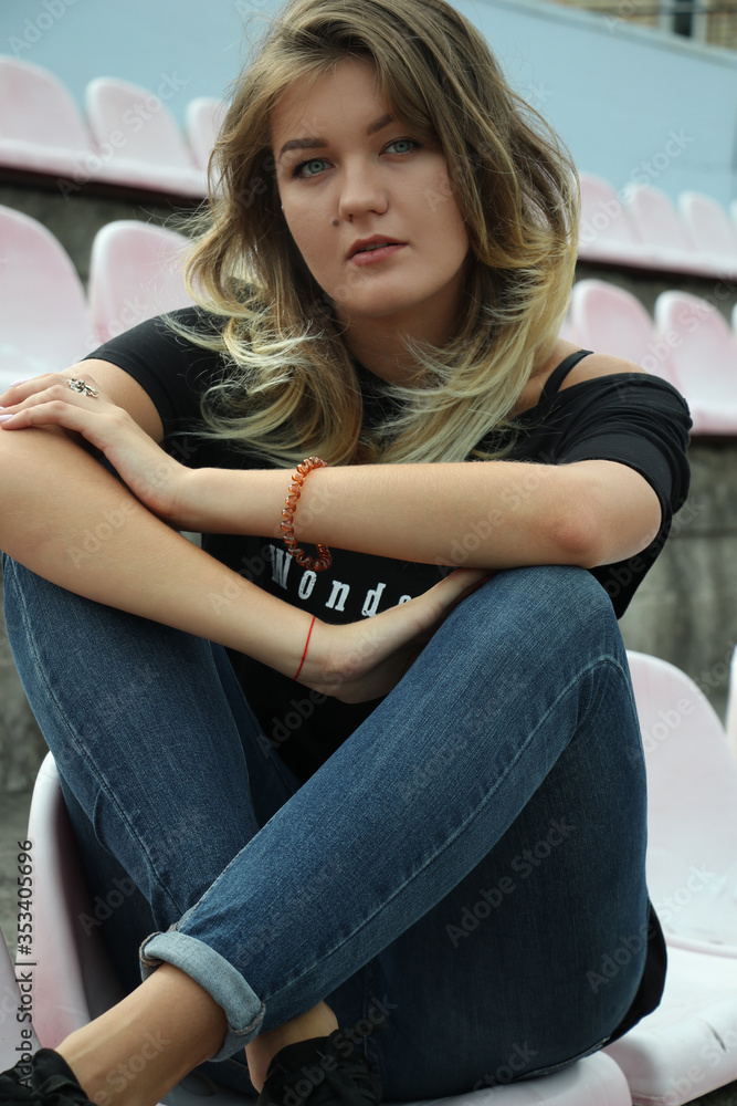 urban portrait of a flirty beautiful woman in black t-shirt and jeans at the stadium, sitting on a bench. urban portrait of a flirty beautiful woman in black t-shirt and jeans at the stadium, sitting on a bench.