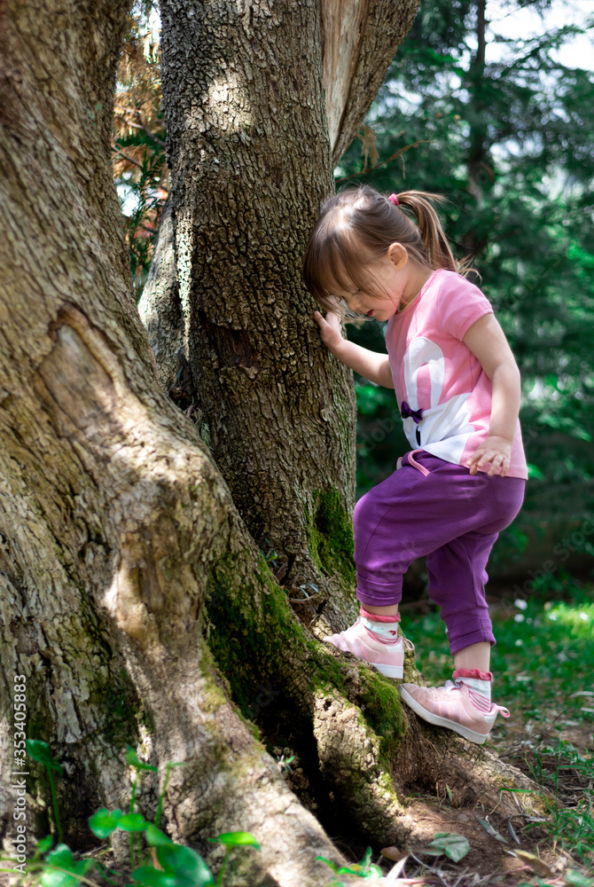 A beautiful little girl wearing colorful clothes climbing a tree in the garden A beautiful little girl wearing colorful clothes climbing a tree in the garden