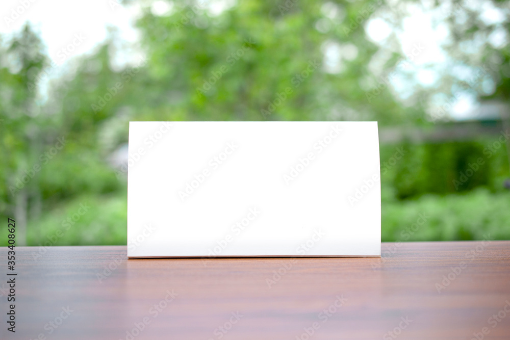 Blank paper Table Tent table-tent on a wooden table with blurred green spring backyard background as template for design presentation, event promotion, showcase etc. Blank paper Table Tent table-tent on a wooden table with blurred green spring backyard background as template for design presentation, event promotion, showcase etc.