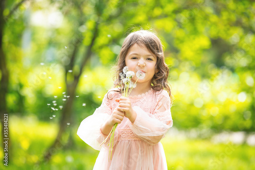 Little girl child cute and beautiful with a bunch of dandelions blowing on them in nature
