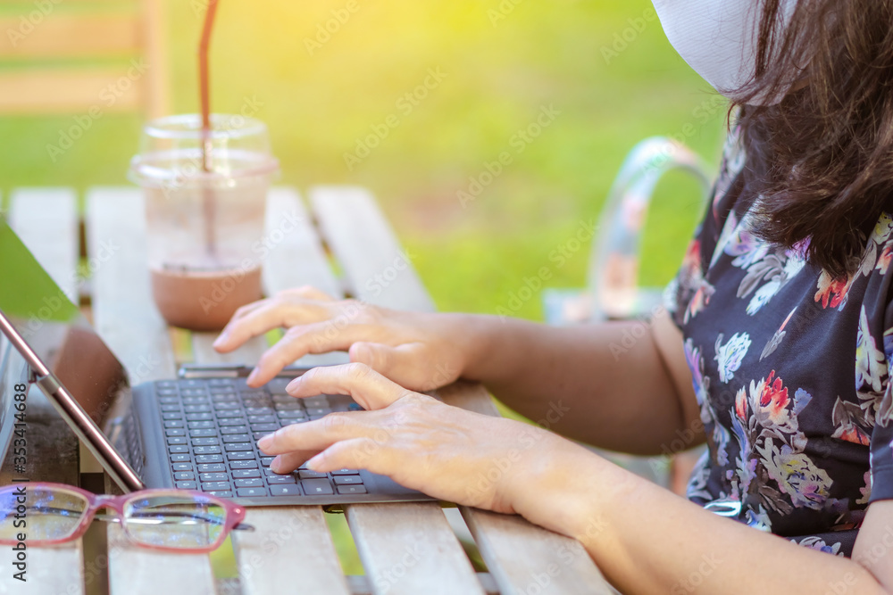 A quarantine woman wear a protective mask to prevent the spread of  of the Corona virus (Covid-19) ,Use a laptop to work from home with green lawn and garden. New normal concept.Selective focus