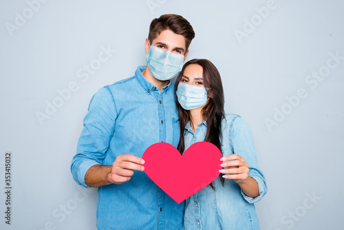 Young happy couple in love story photo shoot holding red paper heart wear medical safety sterile mask on face, social distance pandemic corona virus prevention protection concept covid 19 photo