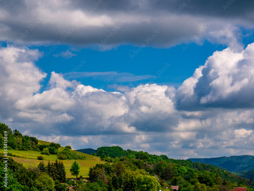 Massive clouds - Cumulus congestus or towering cumulus - forming in the blue sky over hilly landscape