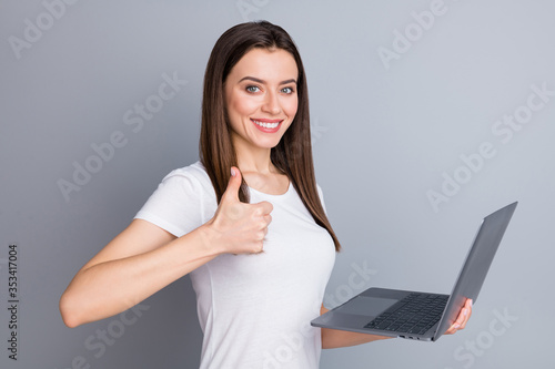 Portrait of confident positive girl manager entrepreneur enjoy corona virus quarantine working home show thumb up sign hold laptop wear white t-shirt isolated over gray color background photo