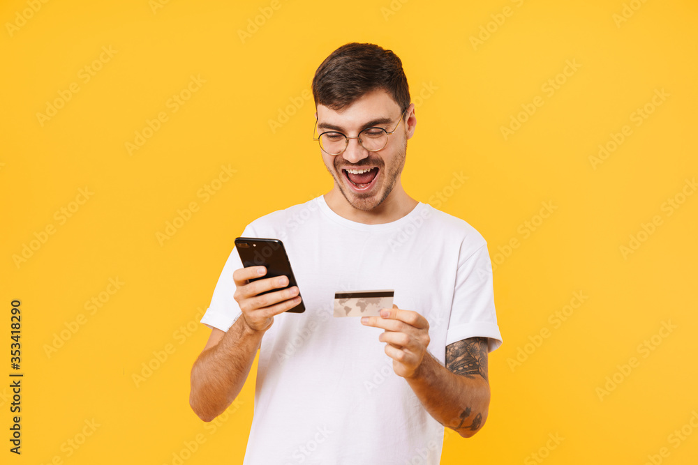 Photo of delighted young man holding credit card and cellphone Photo of delighted young man holding credit card and cellphone