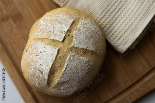 A loaf of homemade sourdough yeast bread boule with a simple cross style scoring technique on a wooden board. Dark and moody style.