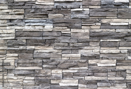 Stone cladding wall made of striped stacked slabs of natural rocks. Colors are dark gray and white, background and texture