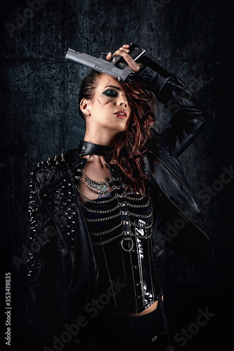 Young woman with scarified face, wearing a studded leather jacket, holding a revolver on her forehead