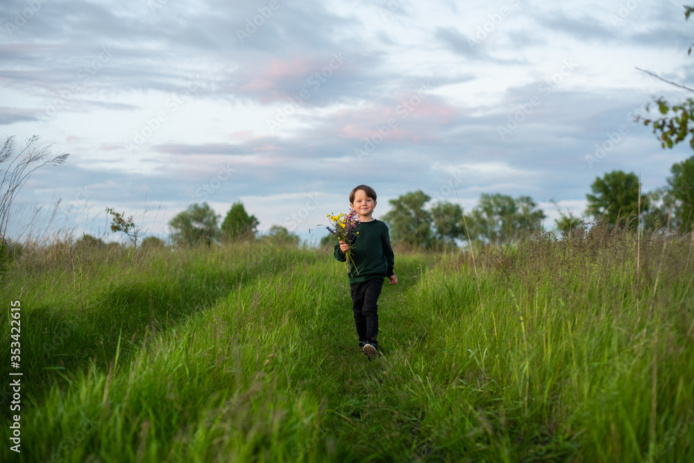 Little smiling boy carries a bouquet of wildflowers in the field