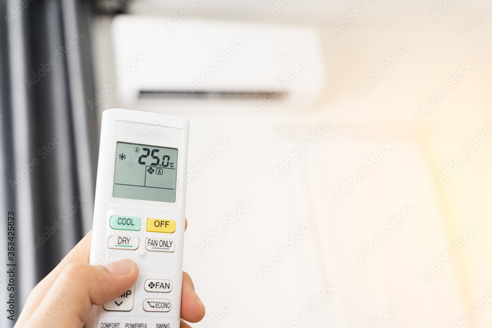 Human hand is using white remote of air conditioner for turn on or adjust temperature of air conditioner inside the room. Human hand is using white remote of air conditioner for turn on or adjust temperature of air conditioner inside the room.