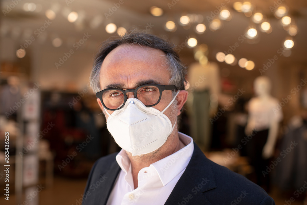 Uomo in giacca con occhiali neri e mascherina protettiva facciale e fermo di fronte a un negozio di abbigliamento