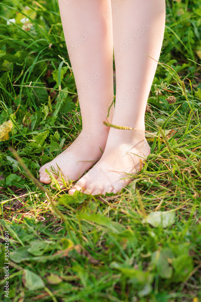 Vertical image of small legs of kid standing on the grass in a nature. Child in nature.