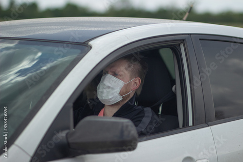 Light man with blue eyes in a medical mask behind the wheel of a car