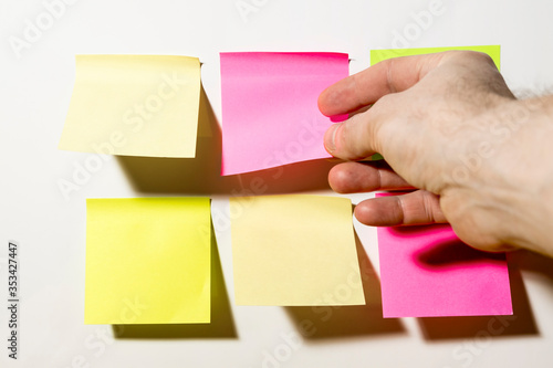 A hand shoots multi-Colored square post-it notes pasted on a white wall