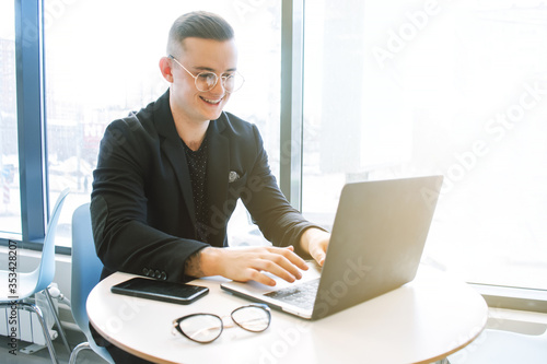 Portrait of a positive looking young business professional working on his laptop with coworkers talking in the background.