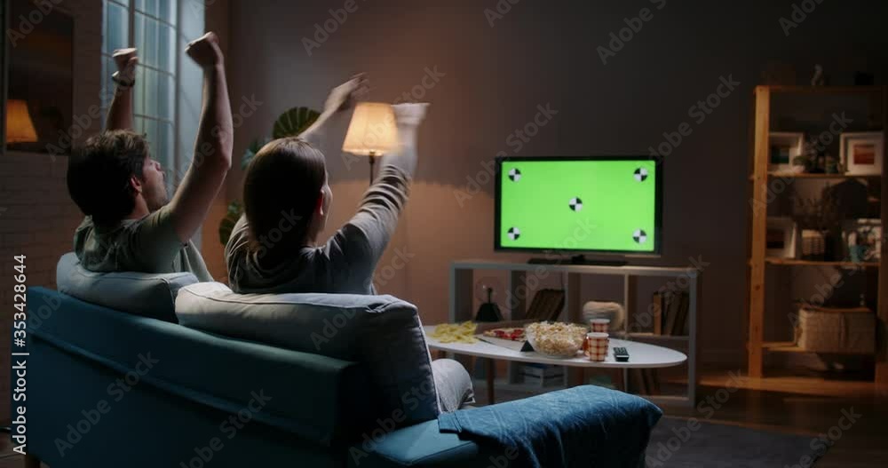 Emotional sports fan couple spending time together watching chroma-key green screen tv and reacting to their team play. 4k footage template Emotional sports fan couple spending time together watching chroma-key green screen tv and reacting to their team play. 4k footage template