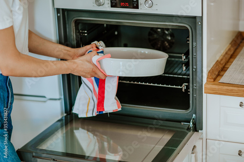 Woman's hands putting white bakery dish into an oven 