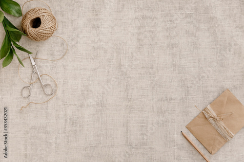 Top view image fashion designer background concept.Flat lay sewing scrapbooking accessory.Scissors, skein of twine, vintage envelope on brown linen fabric at home studio. Space for design mockup