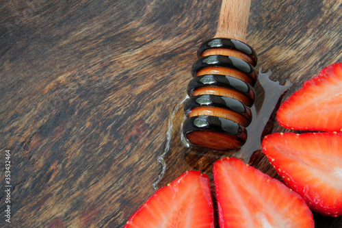 
strawberries on a wooden plate with honey dipper and transparent linden honey. photo