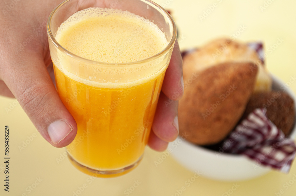 holding a glass of orange juice and brazilian snacks on a yellow background holding a glass of orange juice and brazilian snacks on a yellow background